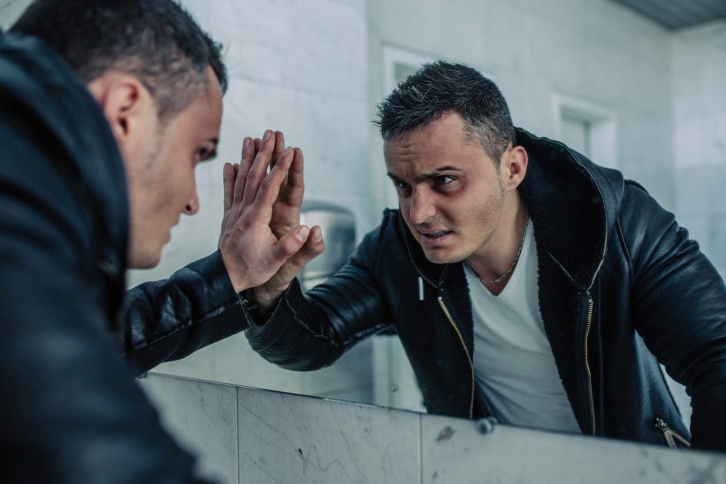 A heroin addict staring at themselves in the mirror, recognizing heroin addiction symptoms and signs.