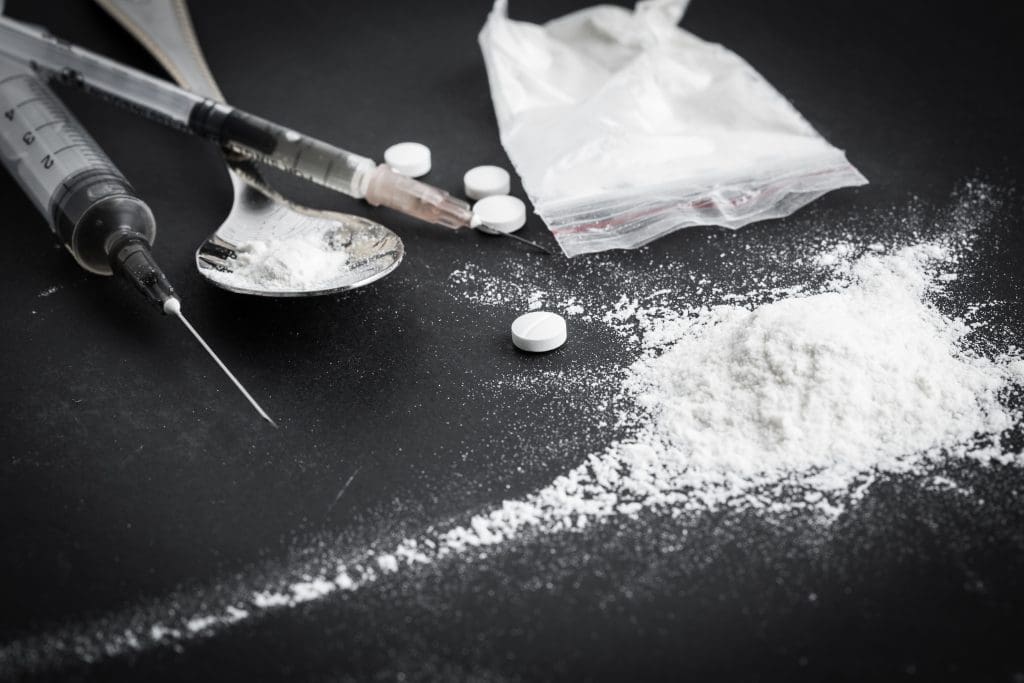 Heroin sprawled out on a table in powder, pill, and syringe form for the heroin addict to choose from.